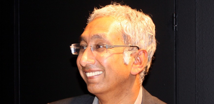 An Asian man with grey hair, wearing glasses and smiling.